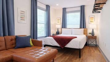 A modern hotel room with a bed, a sofa, a ceiling fan, and a small side table.