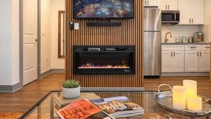 Una cucina moderna con una TV a schermo piatto montata sopra un camino, mobili bianchi e un frigorifero in acciaio inossidabile.