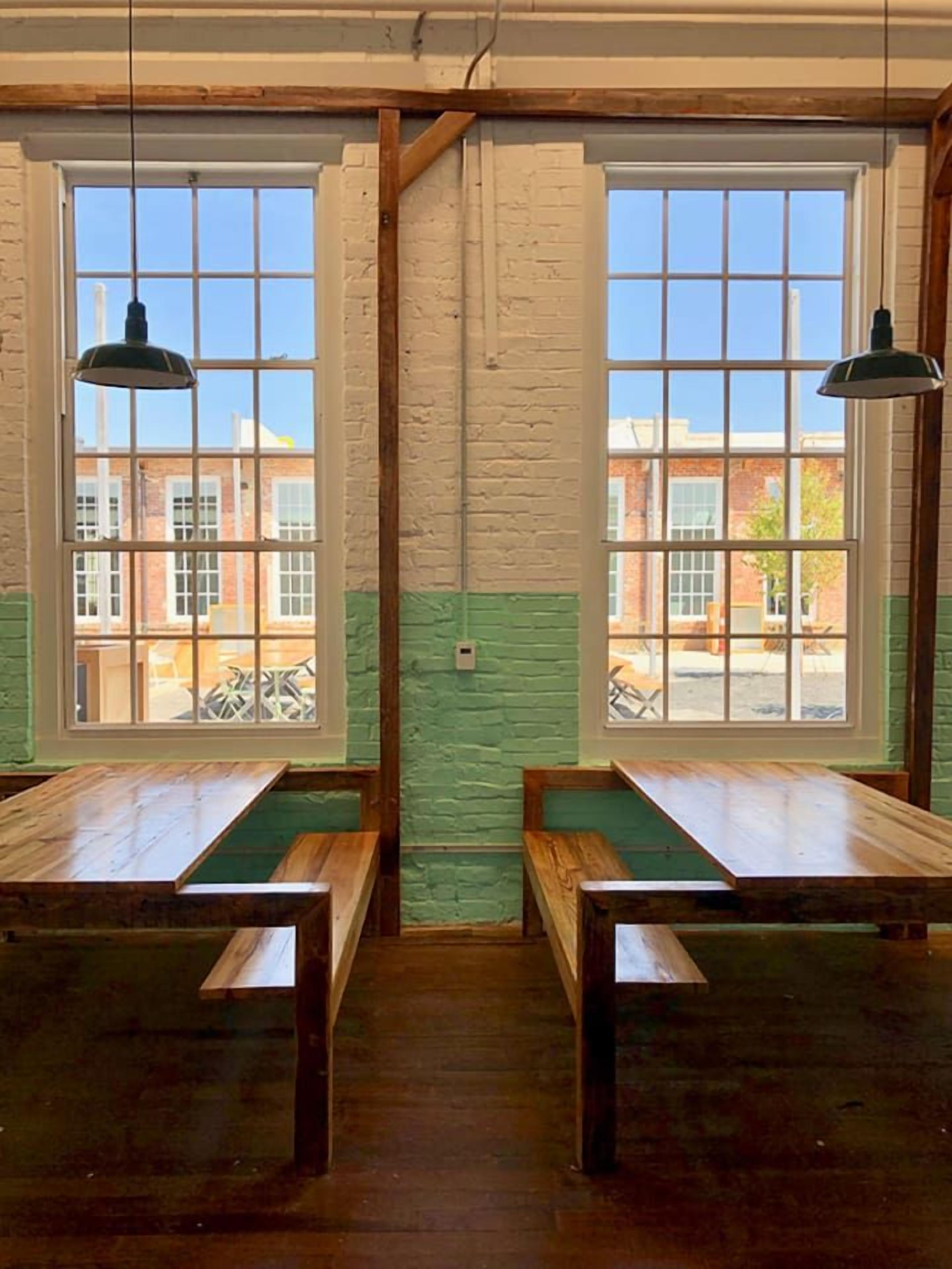 A room with two wooden benches, large windows, and hanging pendant lights.