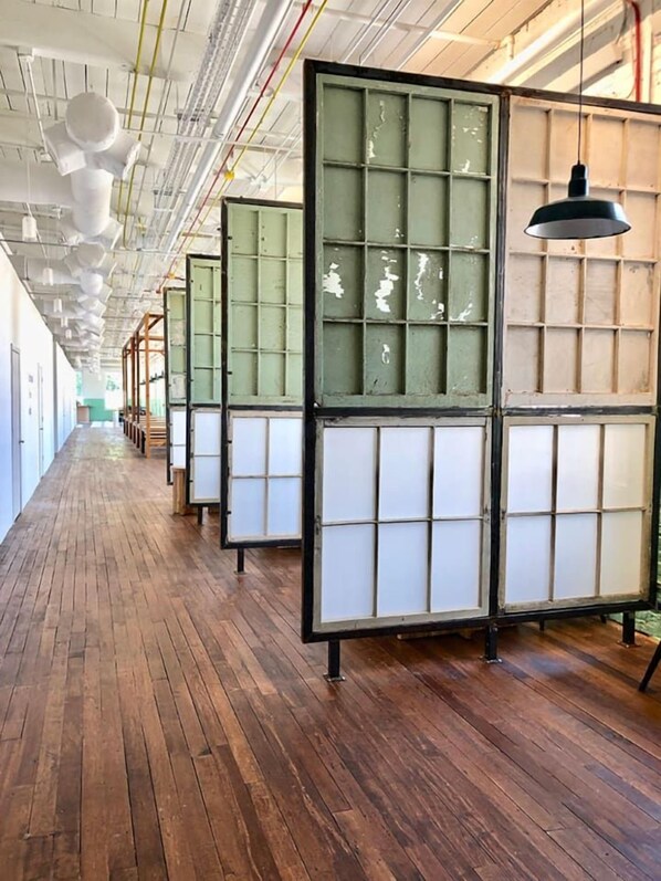 A corridor with wooden flooring and a series of green-framed partitions.