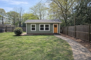 A small, single-story house with a front door and windows, surrounded by a wooden fence and a paved walkway. - Tiny Home Retreat • Greenway • NoDa & Uptown (Charlotte)