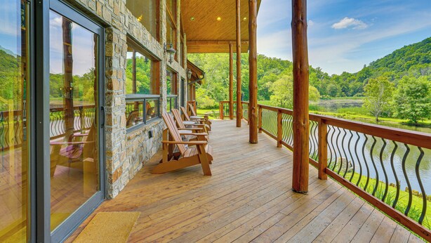 Une terrasse en bois avec des sièges d’extérieur, un mur en pierre et une vue sur un lac et une forêt.