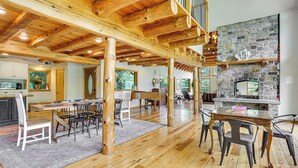 Un intérieur spacieux avec un plafond en bois, une cheminée en pierre et un coin repas comprenant des chaises et une table.