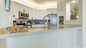 A modern kitchen with white cabinets, stainless steel appliances, and a large island with a bowl of fruit.