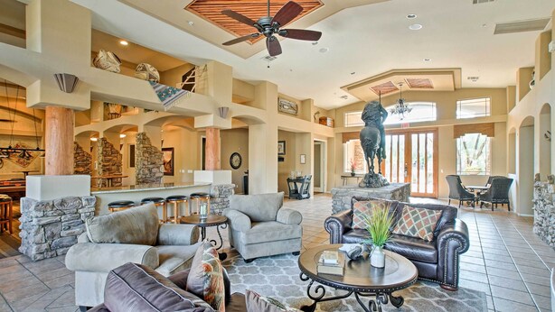 A spacious living area with multiple seating options, a stone fireplace, and a high ceiling with a fan.
