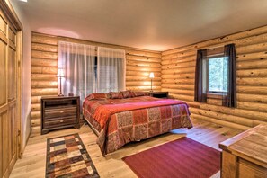 Ein gemütliches Schlafzimmer in einer Blockhütte mit einem großen Bett, Holzwänden, einem Fenster mit Vorhängen und einem Nachttisch mit Lampe.
