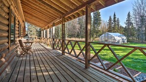 Eine Holzterrasse mit überdachtem Bereich, einem Tisch und Stühlen sowie einem Gewächshaus im Hintergrund.