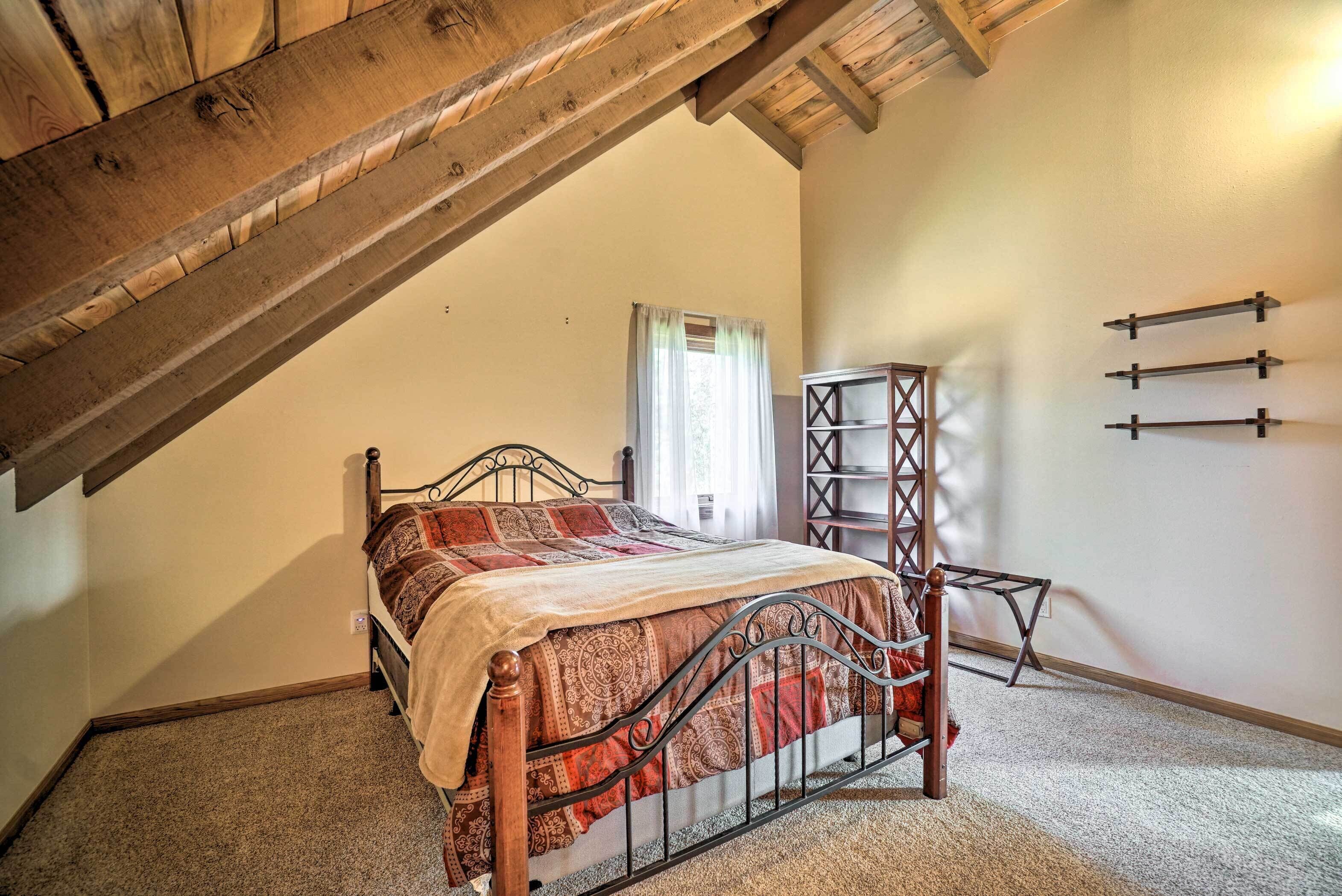 A bedroom with a sloped ceiling, a bed with a patterned bedspread, a wooden ladder, and a small shelf unit against the wall.
