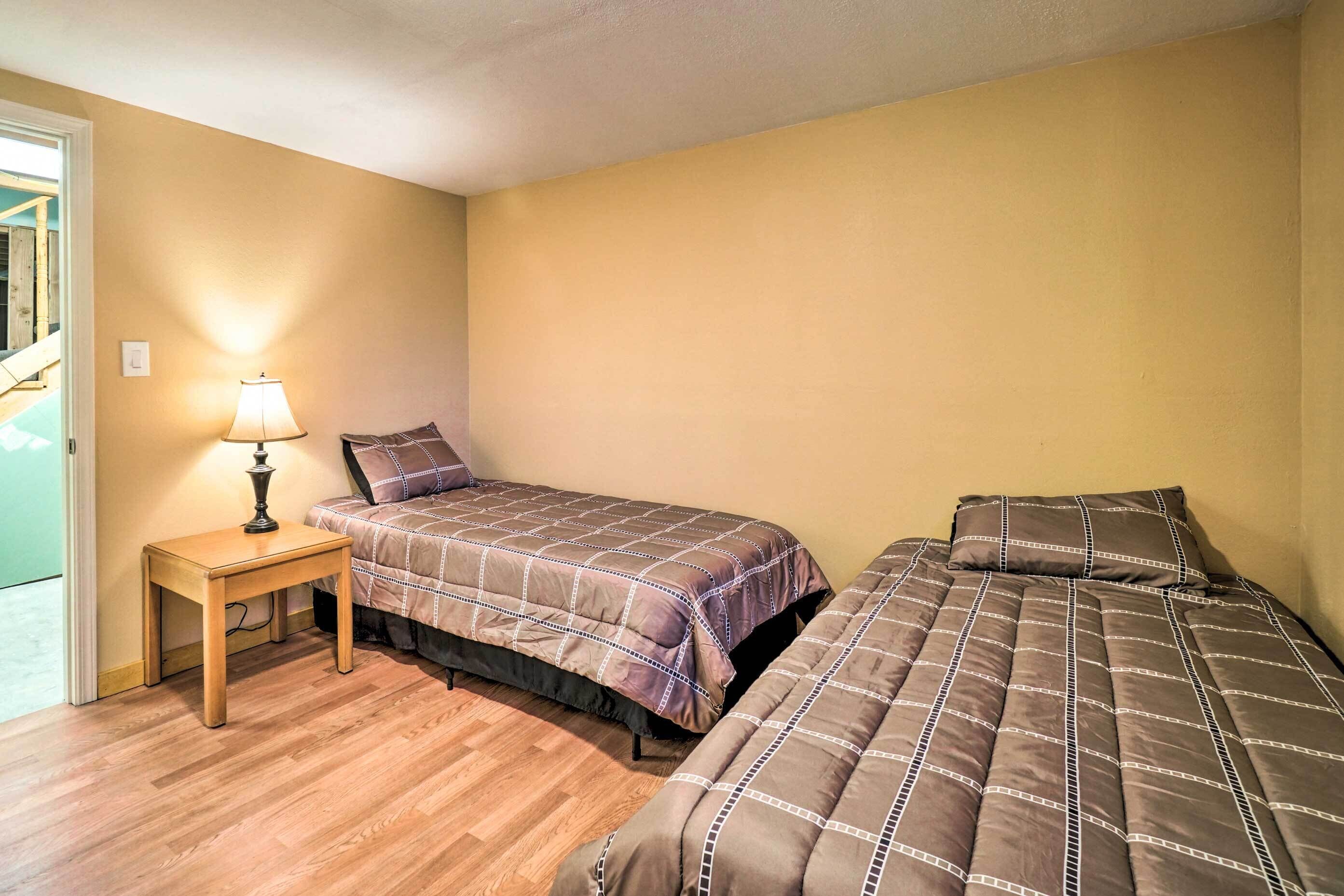 A small, single-bedroom room with two beds, a wooden nightstand with a lamp, and a door leading to a balcony.