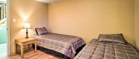 A small, single-bedroom room with two beds, a wooden nightstand with a lamp, and a door leading to a balcony.