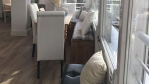 A modern living room with a sofa, chairs, and a dining area. There is a large window with a view of the outdoors.