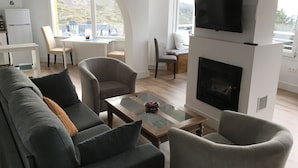 A modern living room with a fireplace, comfortable seating, a dining area, and a large window offering a view of the outdoors.