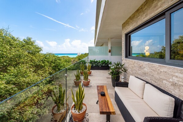 Ein Balkon mit Blick auf den Ozean, Blumentöpfen, einem Holztisch und einer Couch.