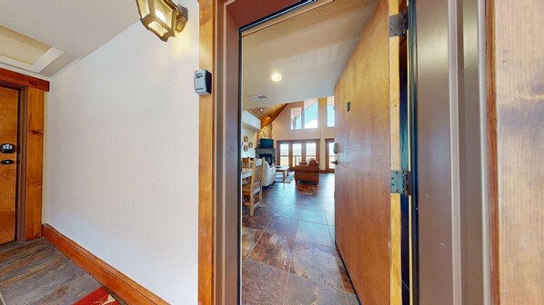 A hallway leading to a living area with a fireplace, wooden flooring, and a view of the outdoors.