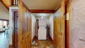 Un couloir étroit aux murs en bois et au sol carrelé, qui mène à une pièce où se trouvent un lave-linge et un réfrigérateur.