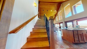 Un escalier en bois mène à une cuisine dotée de grandes fenêtres et d’un plafond haut.