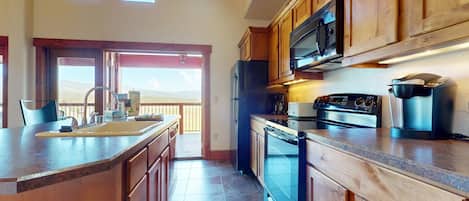 Una cocina con armarios de madera, un refrigerador de acero inoxidable, un microondas, una estufa y una cafetera.