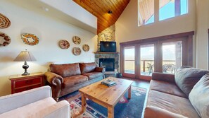 A cozy living room with a stone fireplace, leather sofas, and a wooden ceiling.