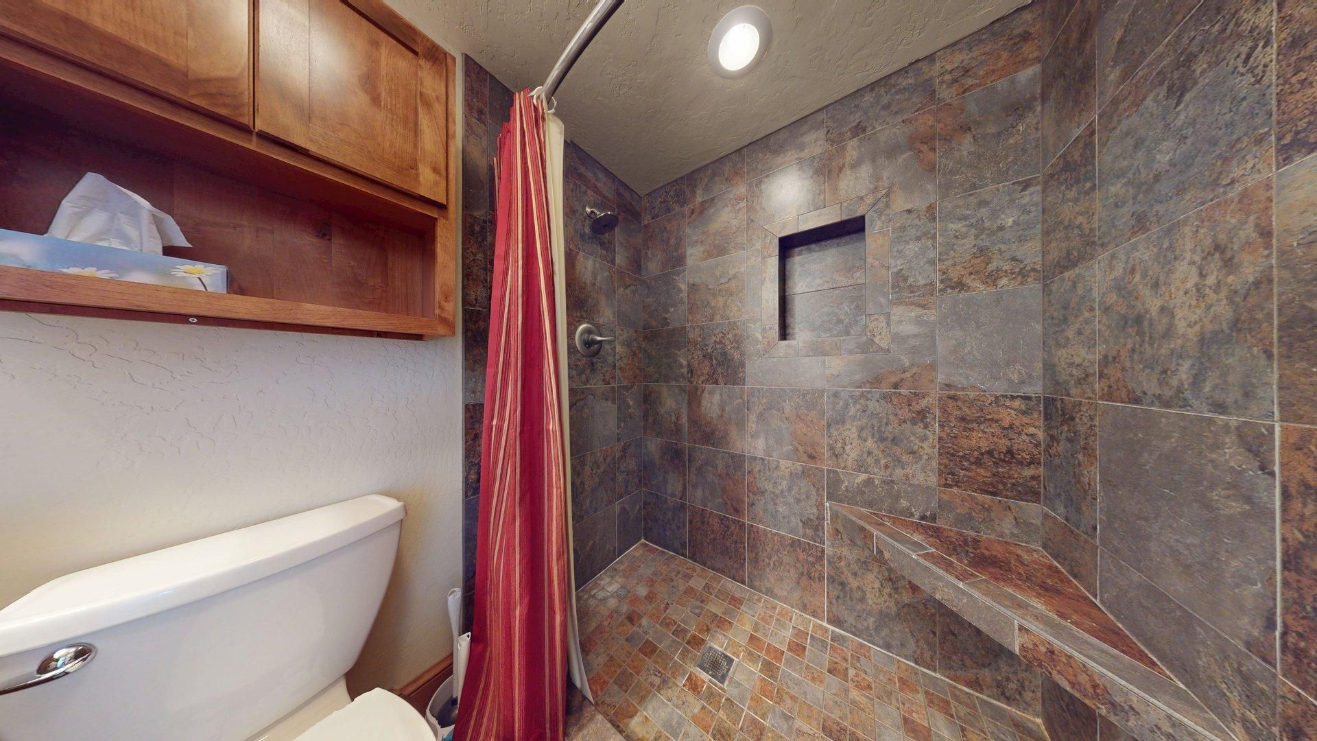 A bathroom with a shower, toilet, and wooden cabinets.