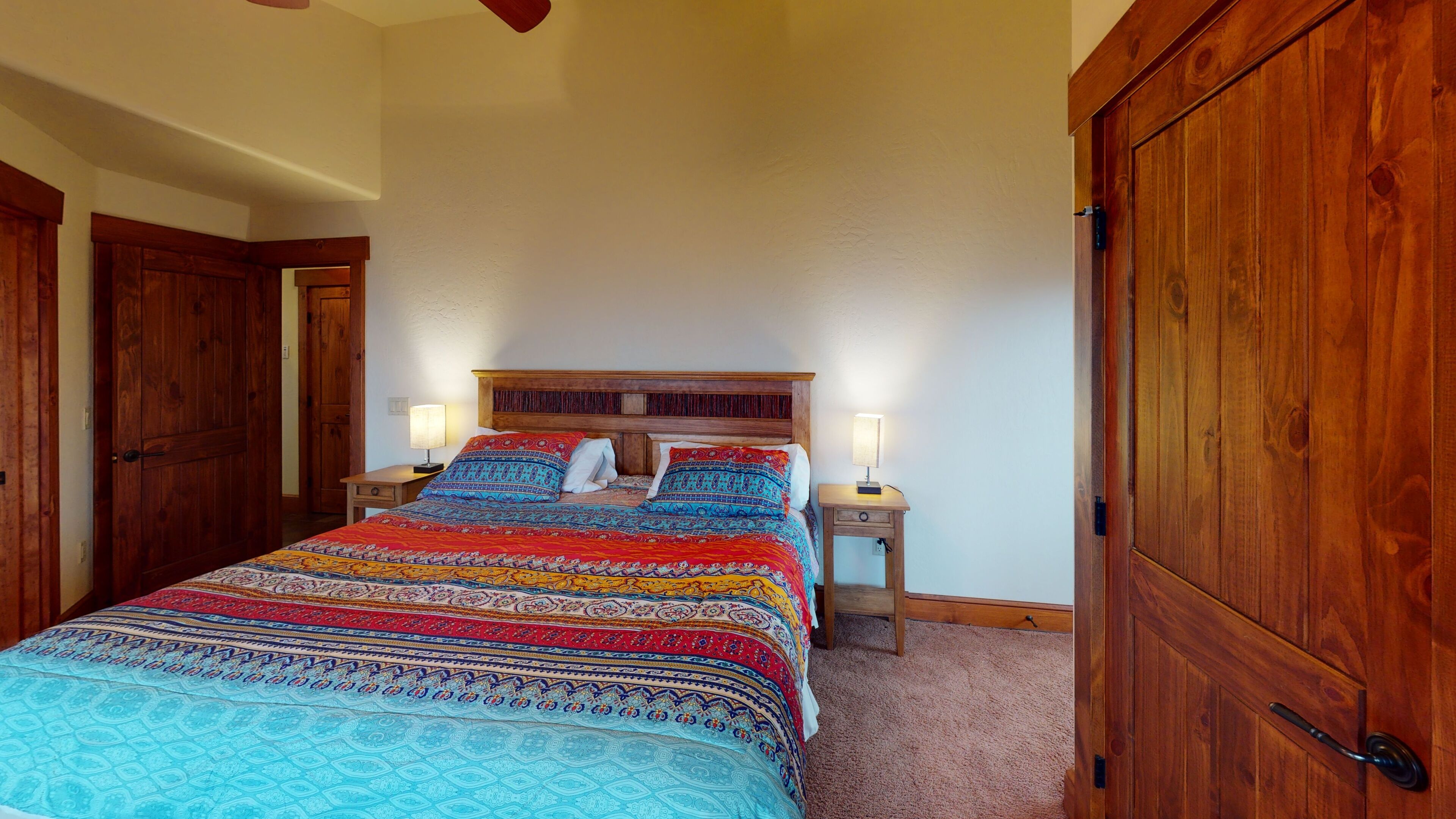 A bedroom with a large bed, wooden wardrobe, and two bedside tables with lamps.