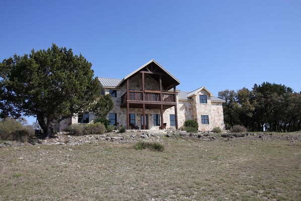A large stone building with a wooden balcony, surrounded by a grassy area and trees. - Beautiful 5/5.5 home on 5 acres w/private pool. River access 2 m. away (Rio Frio)