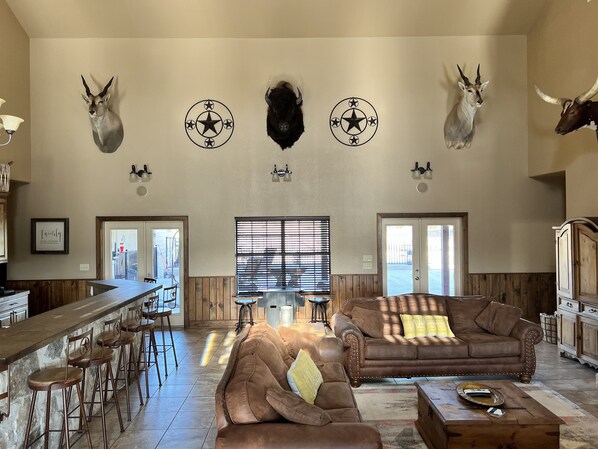 A spacious living area with a bar, leather sofas, and mounted animal heads on the wall.