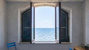 A room with a large arched window overlooking the sea, two blue chairs, and a wooden table. - Cozy home in Tarquinia (VT) with WiFi (Tarquinia (VT))
