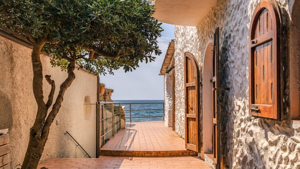 A narrow stone pathway leading to a wooden door, flanked by a tree and a building with a stone facade. - Cozy home in Tarquinia (VT) with WiFi (Tarquinia (VT))