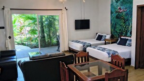 A hotel room with a ceiling fan, a TV, a mural, a sofa, a bed, and a dining table. - Hotel & Suites Oasis Bacalar (Bacalar)