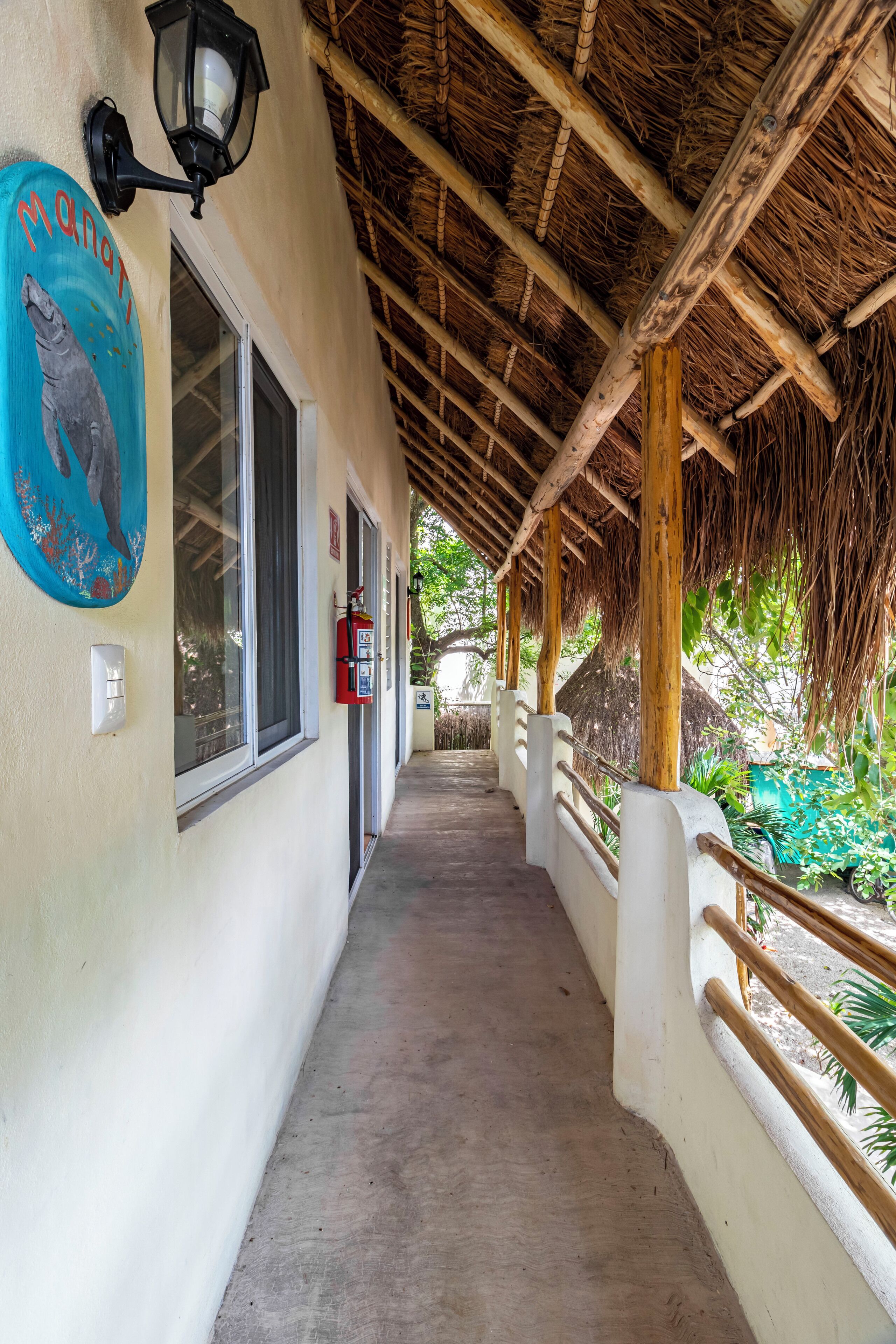 A covered walkway with a thatched roof, a fire extinguisher, and a mural on the wall.