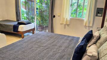 Un dormitorio con una cama grande, un sofá, un ventilador de techo y vistas al exterior a través de una puerta corredera.