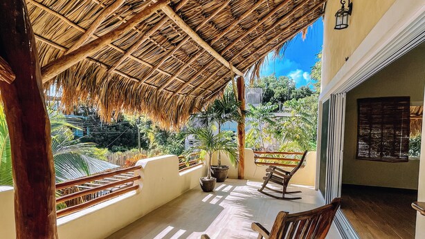A covered outdoor area with a thatched roof, wooden chairs, and a view of greenery. - Hotel & Suites Oasis Bacalar (Bacalar)