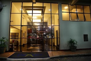 A hotel entrance with a glass door, a reception desk inside, and potted plants outside. - Dexter Hotel (Volta Redonda)