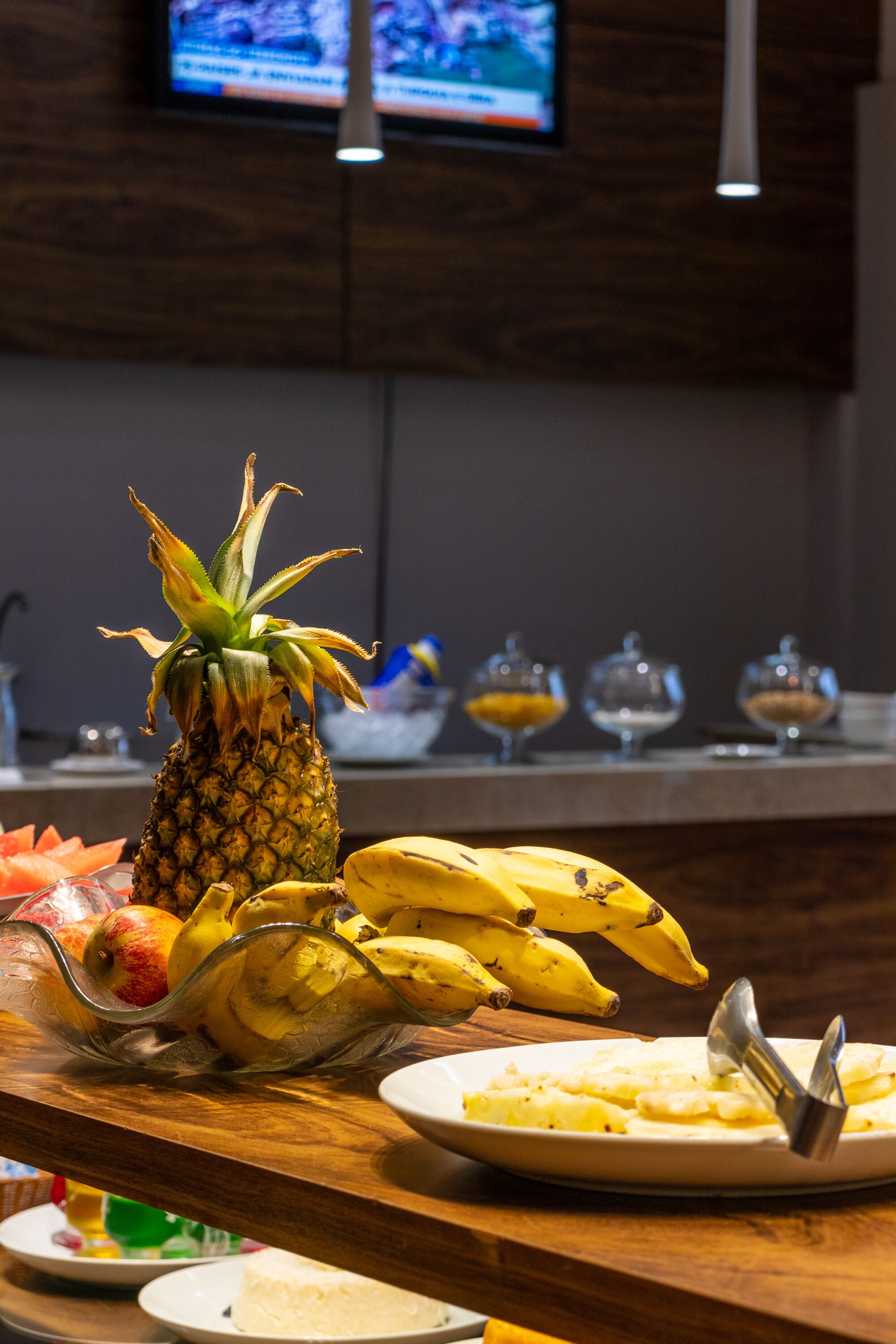 A breakfast bar with a pineapple, bananas, and a plate of pancakes.