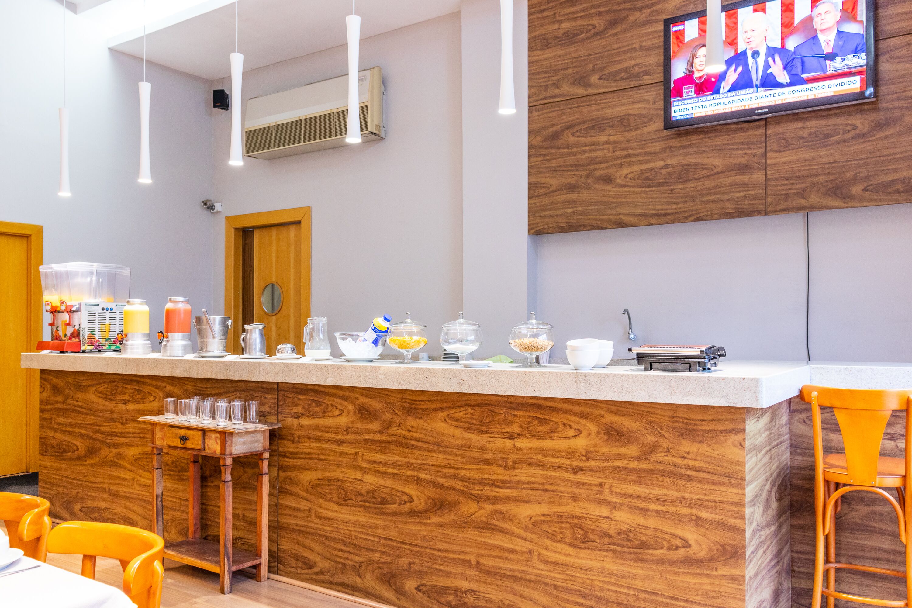 Zona de bar moderna con mostrador de madera, taburetes y una pantalla de televisión mostrando un noticiero.