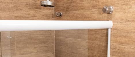 A shower with a chrome showerhead and control knobs, set against a wooden wall with a white horizontal bar above.