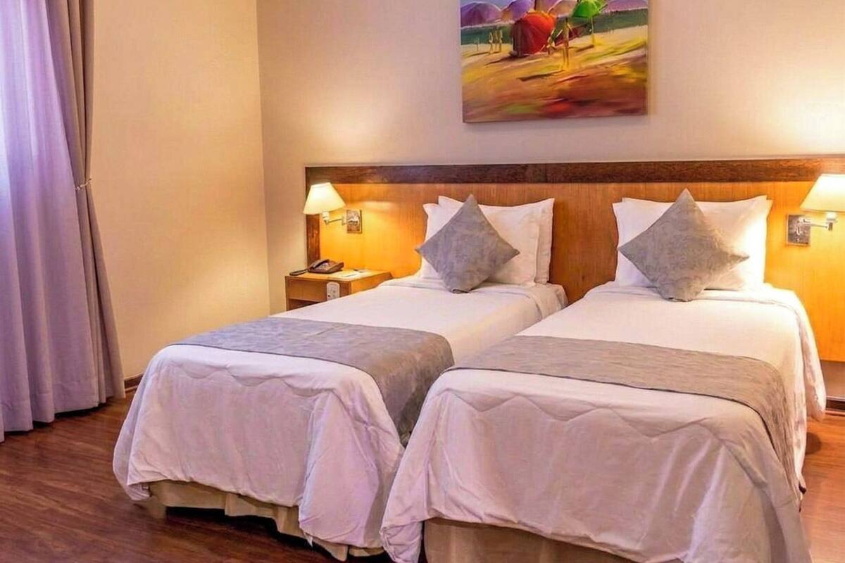 A hotel room with two beds, a wooden headboard, bedside lamps, and a painting on the wall.