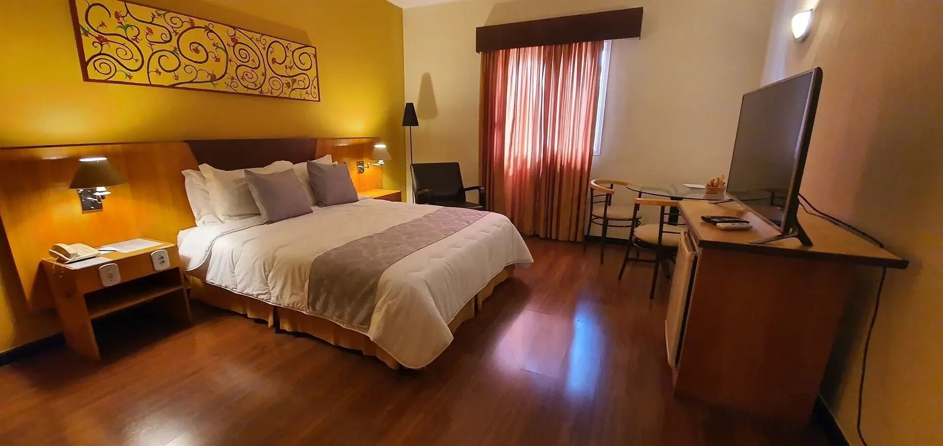 A hotel room with a bed, desk, chair, lamp, and TV.