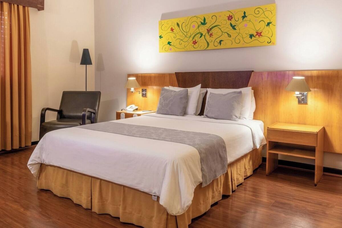 A hotel room with a large bed, two bedside tables, a chair, and a wall-mounted artwork.