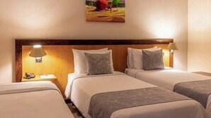 A hotel room with three single beds, a wooden headboard, bedside lamps, a painting on the wall, and a small table with a phone and notepad. - Dexter Hotel (Volta Redonda)