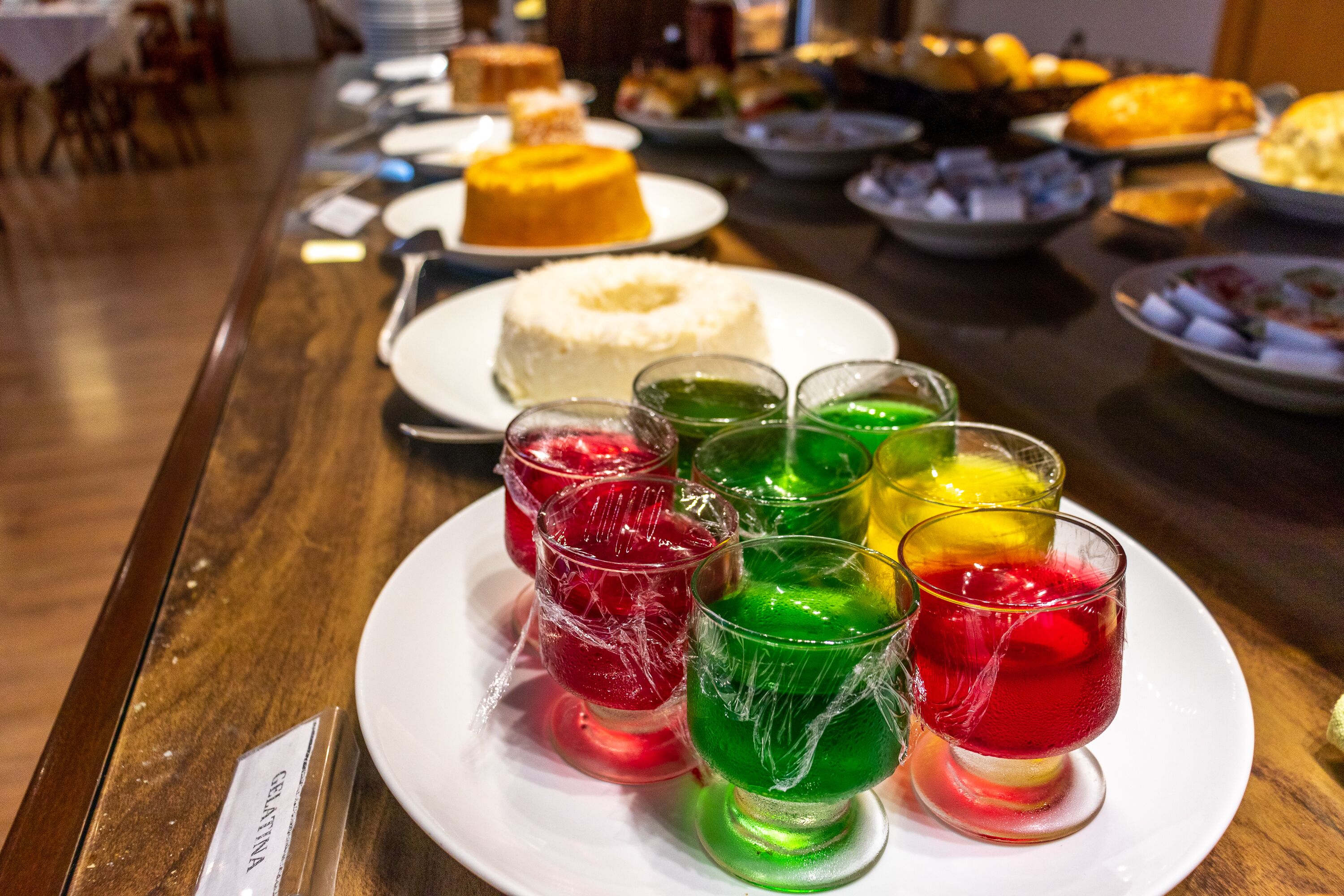 A table with various desserts and drinks, including a white cake and colorful gelatin cups.