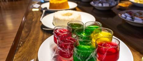 A table with various desserts and drinks, including a white cake and colorful gelatin cups.