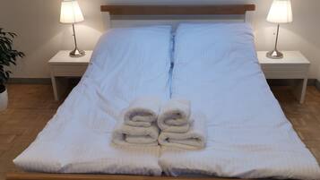 A neatly made bed with white linens and rolled towels, flanked by two bedside lamps on matching nightstands.