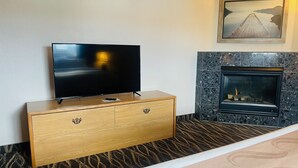 Habitación de hotel con televisión de pantalla plana sobre un mueble de madera, chimenea y un cuadro enmarcado encima de la chimenea.