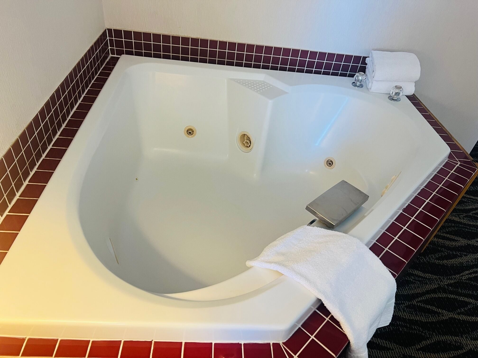 Una bañera grande y vacía con interior blanco y un revestimiento de azulejos rojos.