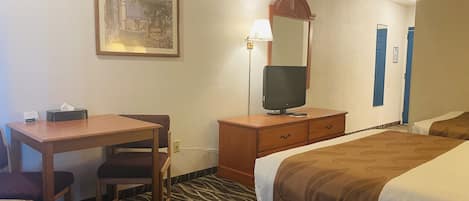 A hotel room with a bed, a desk with a chair, a television, a mirror, and a framed picture on the wall.