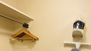 Una habitación con un perchero de madera, una tabla de planchar blanca y un enchufe con cable.
