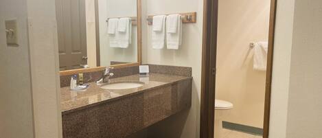 A bathroom with a granite countertop, two sinks, a mirror, and a toilet.