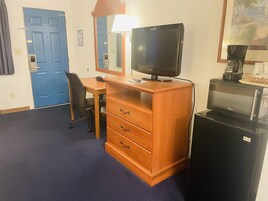Habitación de hotel con escritorio de madera, televisor, cafetera y microondas.