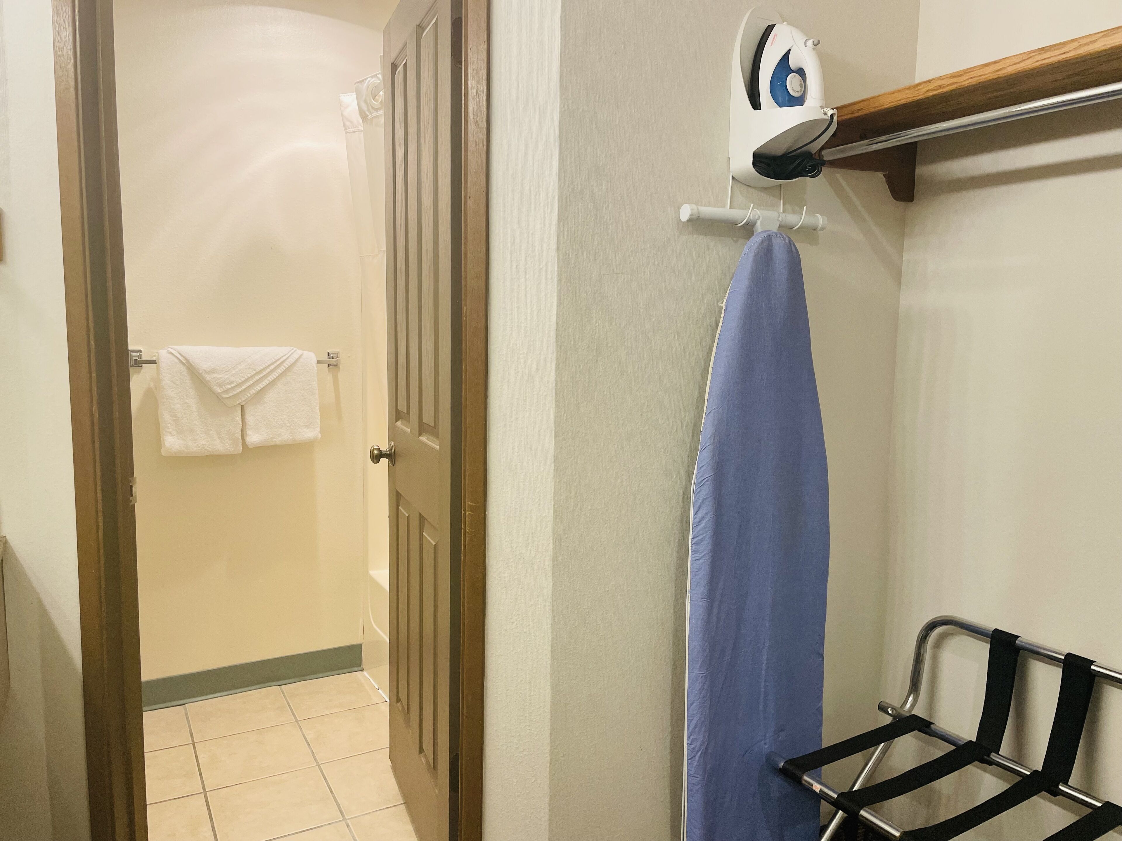A bathroom with a shower curtain, a towel rack with towels, and an iron on a wall-mounted rack.
